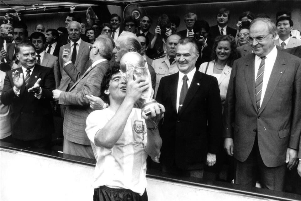 29.6.1986: Der argentinische Fußballstar Diego Maradona jubelt mit dem eroberten Weltmeisterschaftspokal - der mexikanische Staatspräsident Miguel de la Madrid (2. von rechts) und Bundeskanzler Helmut Kohl (rechts) schauen zu. (Archivbild)dpa/Picture-Alliance/dpa