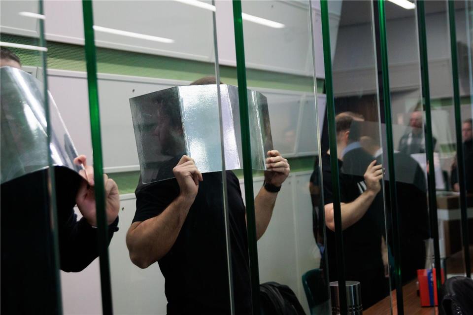 Angeklagte verdecken ihre Gesichter im Gerichtssaal beim Prozess wegen mehrerer Fahrzeugbrände. (Archivbild) Carsten Koall/dpa