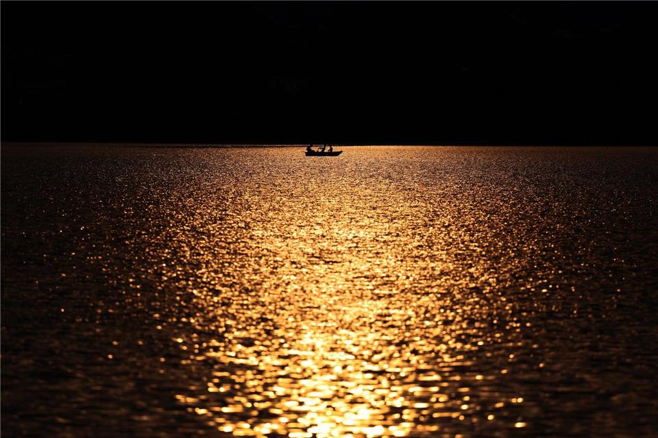 Angler rudern in einem Kahn über den im Sonnenuntergang glitzernden Hopfensee.Karl-Josef Hildenbrand/dpa
