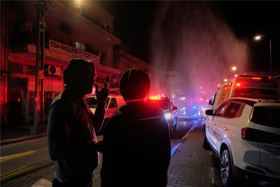 Anwohner beobachten die Arbeit der Rettungskräfte am Ort eines Raketeneinschlags in Tel Aviv.Maya Levin/AP/dpa