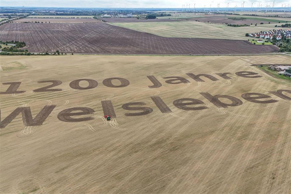 Auf einem Acker steht „1200 Jahre Welsleben“ - gezogen mit einem Traktor. Peter Gercke/dpa