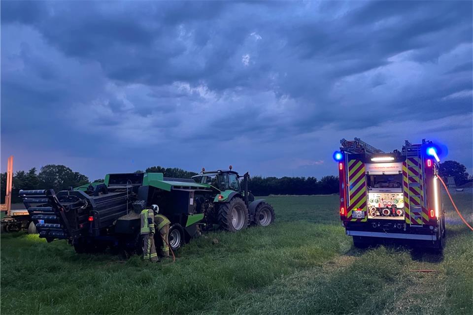 Auf einem Feld in Raesfeld ist eine Strohpresse in Brand geraten. Die Einsatzkräfte prüfen die Temperatur der Bremsen.