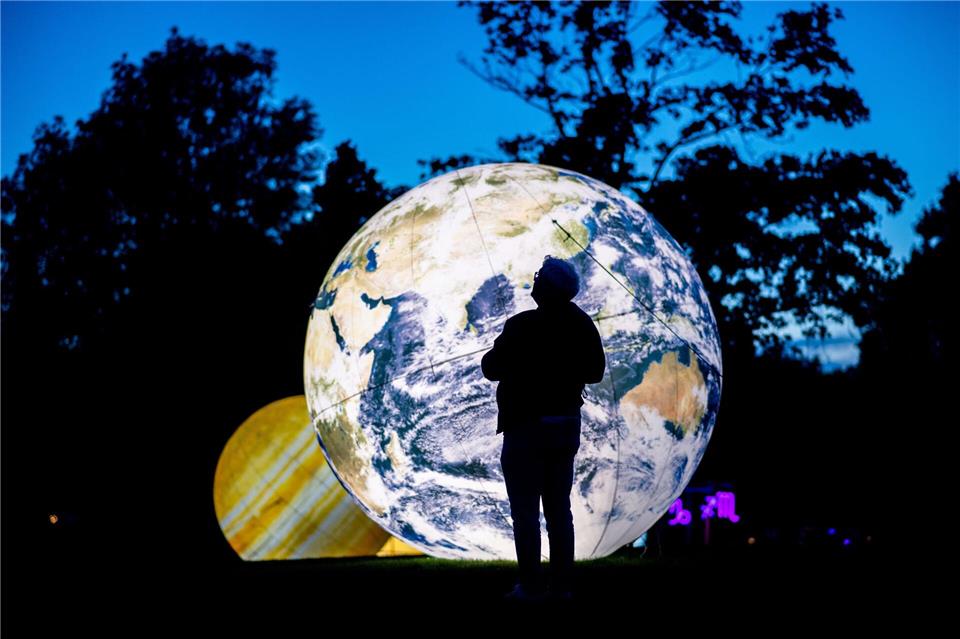 Auf einer Wiese im Park sind metergroße, beleuchtete Planeten zu sehen. Hauke-Christian Dittrich/dpa
