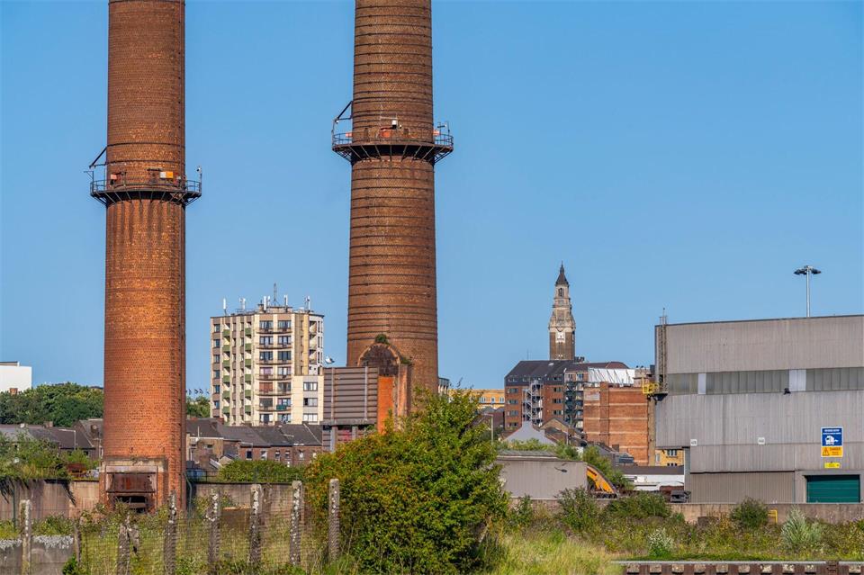 Aufgegebene Schornsteine - Relikte der Schwerindustrie vor Wohnhäusern und Glockenturm in Charleroi.Oliver Gerhard/dpa-tmn