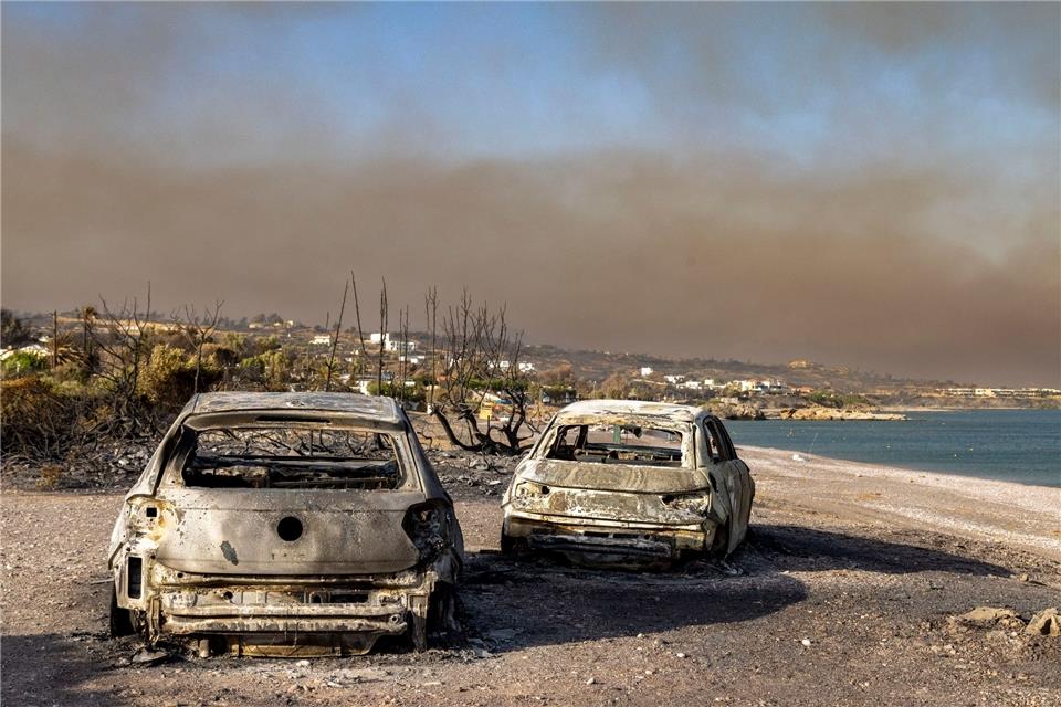 Rhodos kämpft gegen das Feuer - und bangt um Tourismuus Ausgebrannte Autos am Strand von Kiotari. Im Hintergrund ist eine riesige Rauchwolke zu sehen.