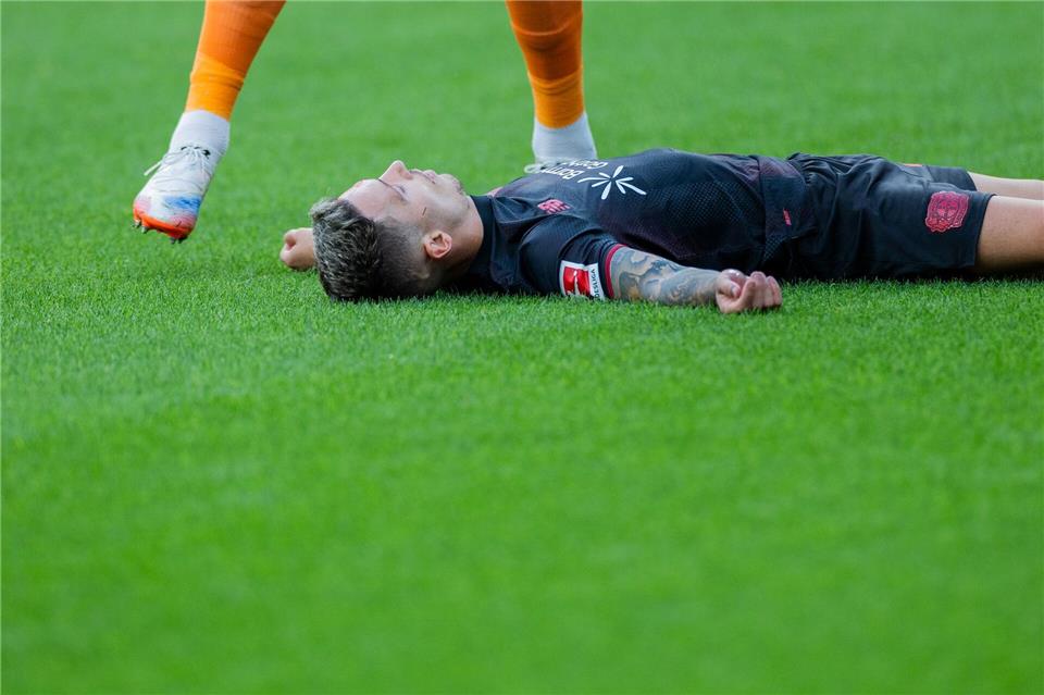 Bayer Leverkusens Kapitän Alejandro Grimaldo liegt nach einem Zusammenprall mit dem eigenen Mann benommen auf dem Boden. Rolf Vennenbernd/dpa