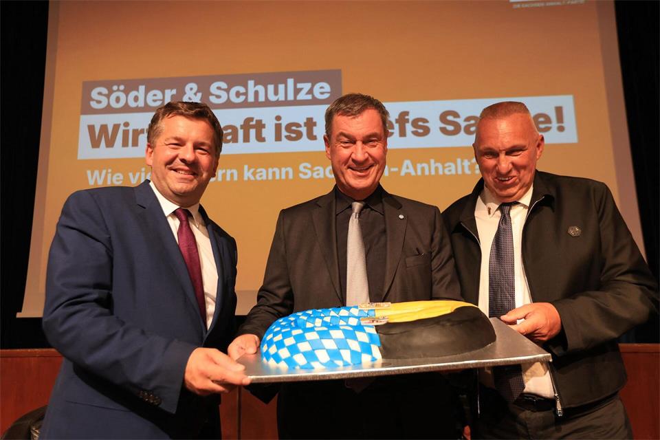 Bayerns Ministerpräsident Markus Söder (M, CSU) bekommt während einer Wahlkampfveranstaltung von Sachsen-Anhalts Landeskonditormeister Michael Wecker (r) eine Brezel in den Farben der Bundesländer Bayerns und Sachsen-Anhalts überreicht.Matthias Bein/dpa