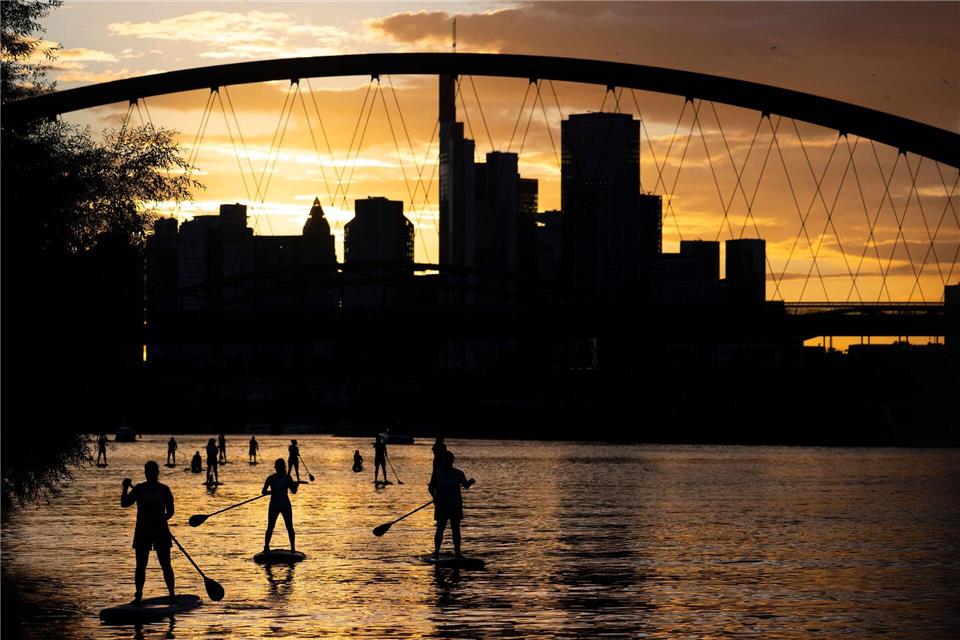 Bei Sicht auf die Skyline im letzten Licht des Tages fahren Stand-Up-Paddler in Nähe der Frankfurter Osthafenbrücke über den Main.Boris Roessler/dpa