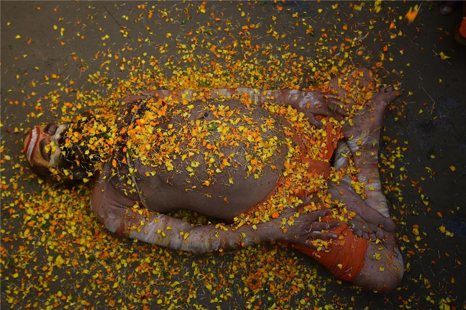 Bei einem hinduistischen Frühlingsfest in Indien liegt ein Sadhu mit Blütenblättern bedeckt auf der Straße. Prabhat Kumar Verma/ZUMA Press Wire/dpa