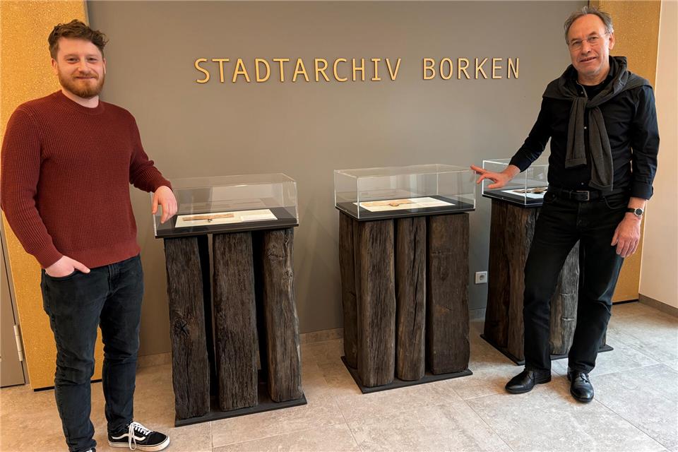 Bernd Schmäing (links) und sein Vorgänger Dr. Norbert Fasse vor den repräsentativen Vitrinen im Foyer des neuen Stadtarchivs. Sie sind aus historischen Eichenbohlen gefertigt, die man bei Ausgrabungen am Mühlentor fand.