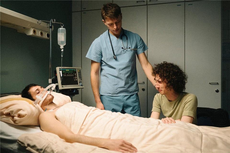 Bernhard Hoestermann (Clemens Bobke, Mitte) pflegt Heiko (Evangelos Tsarkowistas, links) während Dirk (Benjamin Viziotis, rechts) an seinem Bett sitzt - nachgespielte Szene aus dem zweiten Teil der ZDF-Dokuserie „AIDS - In Zeiten der Liebe“.Elliott Kreyenberg/ZDF/dpa