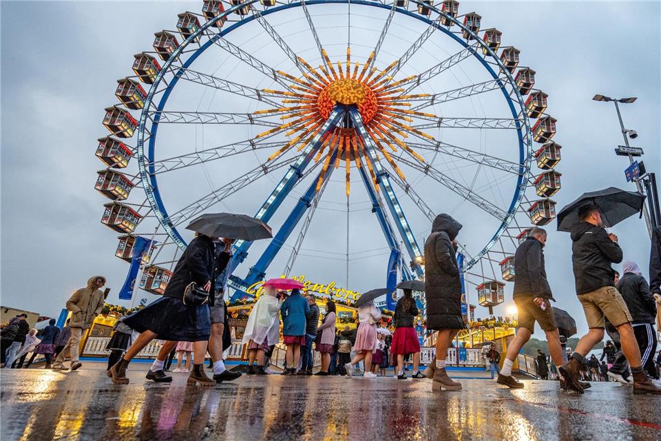 Besucher des Oktoberfestes in München gehen im Regen über das Festgelände vor dem Riesenrad.Armin Weigel/dpa