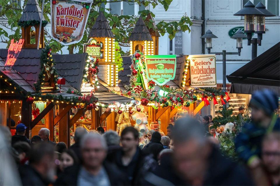Besucher gehen an beleuchteten Verkaufshütten vorbei.Christoph Reichwein/dpa