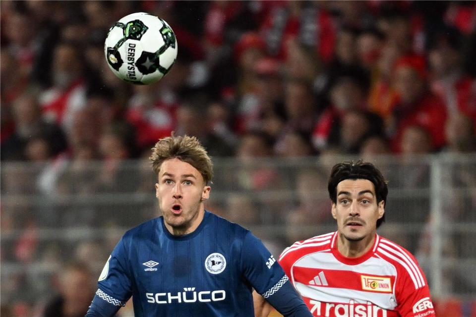 Union mit Zittersieg gegen Pokal-Schreck Bielefeld Bielefelds Kunze (l.) und Union Leite (r.) visieren den Ball an. Soeren Stache/dpa
