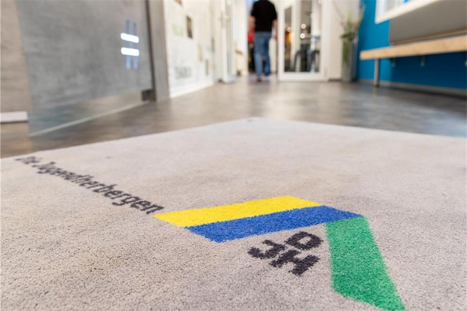 Blick auf den Teppich am Eingang einer Jugendherberge mit Logo des Deutschen Jugendherbergswerks (DJH).