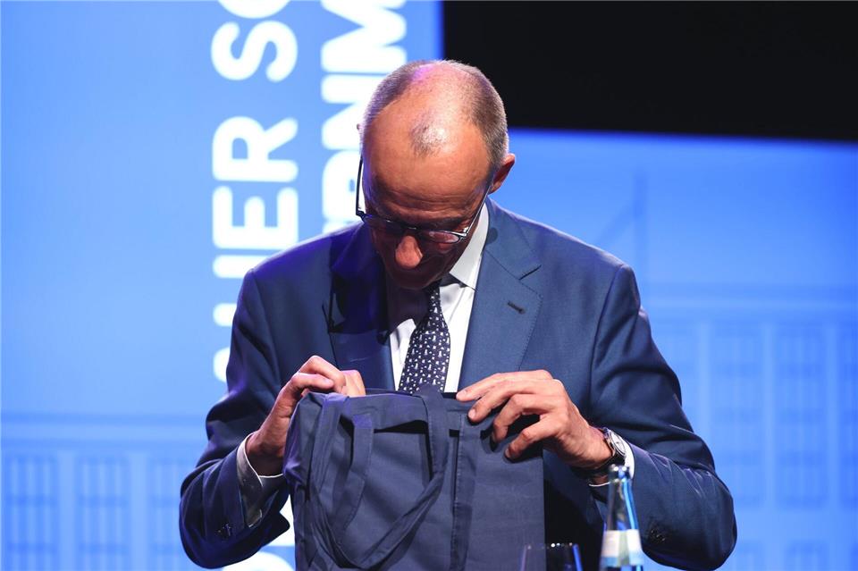 Bundeskanzler Friedrich Merz bekam nach seiner Festrede an der Universität Köln eine Geschenktasche überreicht. Rolf Vennenbernd/dpa