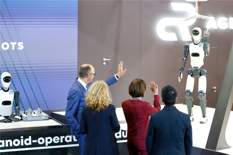 Bundeskanzler Friedrich Merz winkt einem Roboter zu – die Zukunft winkt zurück.Michael Matthey/dpa