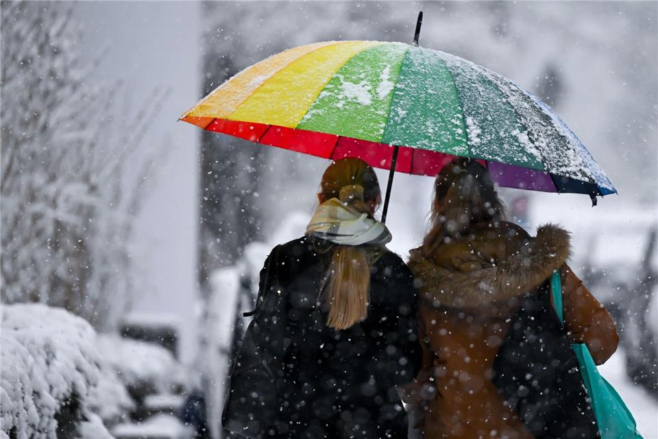 Bunt und grau zugleich: Zwei Frauen gehen mit einem Schirm bei Schneefall in München.Sven Hoppe/dpa