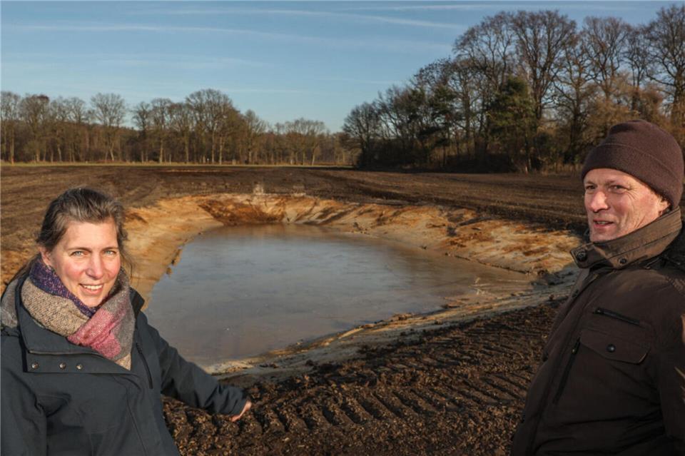 Caroline Bücher und Rainer Ebbing stehen vor der Blänke, die in der warmen Jahreszeit Insekten anlocken soll. Die Böschung ist so flach, dass auch Amphibien sie bewältigen können. Derzeit ist die Wasseroberfläche gefroren.