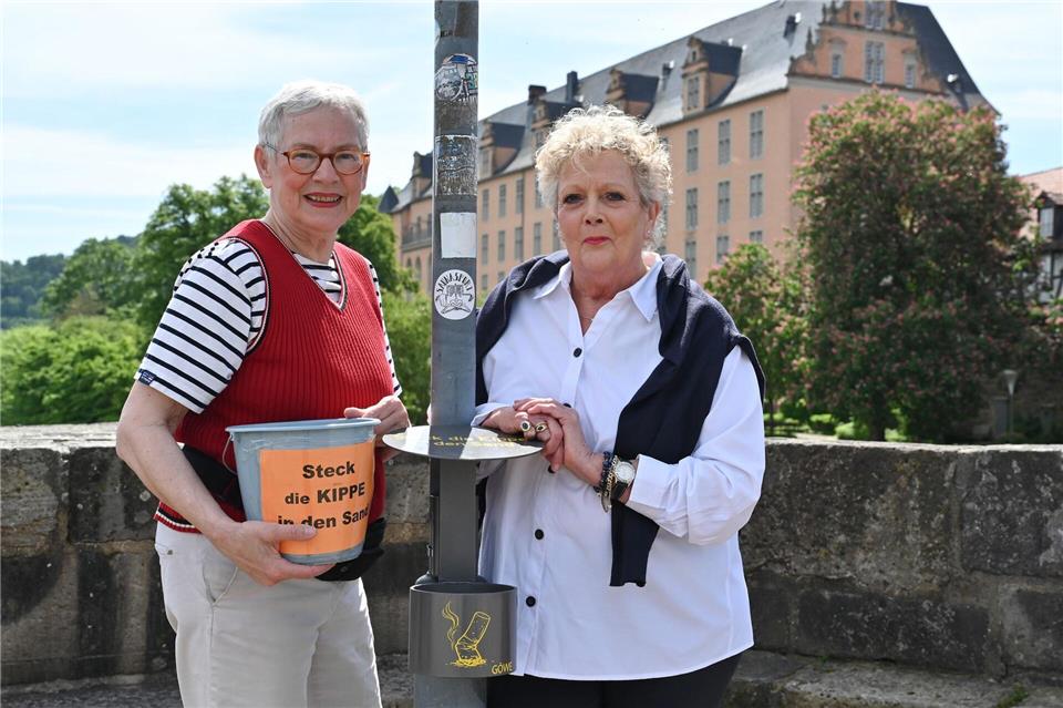 Cornelia Schulze (l) und Heike Tauer-Schneider haben in einer Nacht und Nebelaktion Plastikeimer als Kippen-Mülleimer aufgestellt. Nun gibt es eine Dauerlösung.Swen Pförtner/dpa