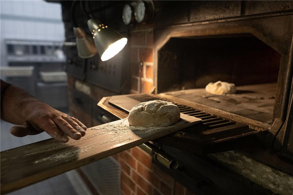 Das Einbringen eines geformten Teiglings in den heißen Backofen mit Hilfe eines Brotschiebers wird „Einschießen“ genannt. Oft wird der Vorgang von einem kurzen Ruck begleitet, damit das Brot auf dem Backstein oder Backblech landet. Swen Pförtner/dpa/dpa-tmn