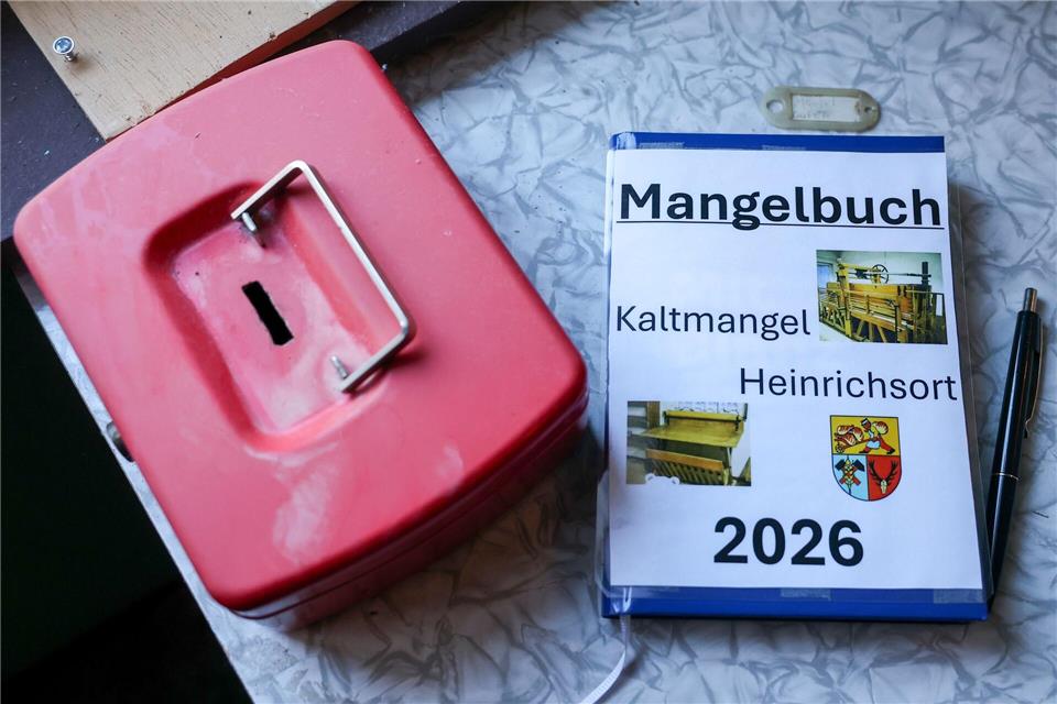Das Mangelbuch und die Kasse liegen neben einer historischen Kaltmangel. Jan Woitas/dpa