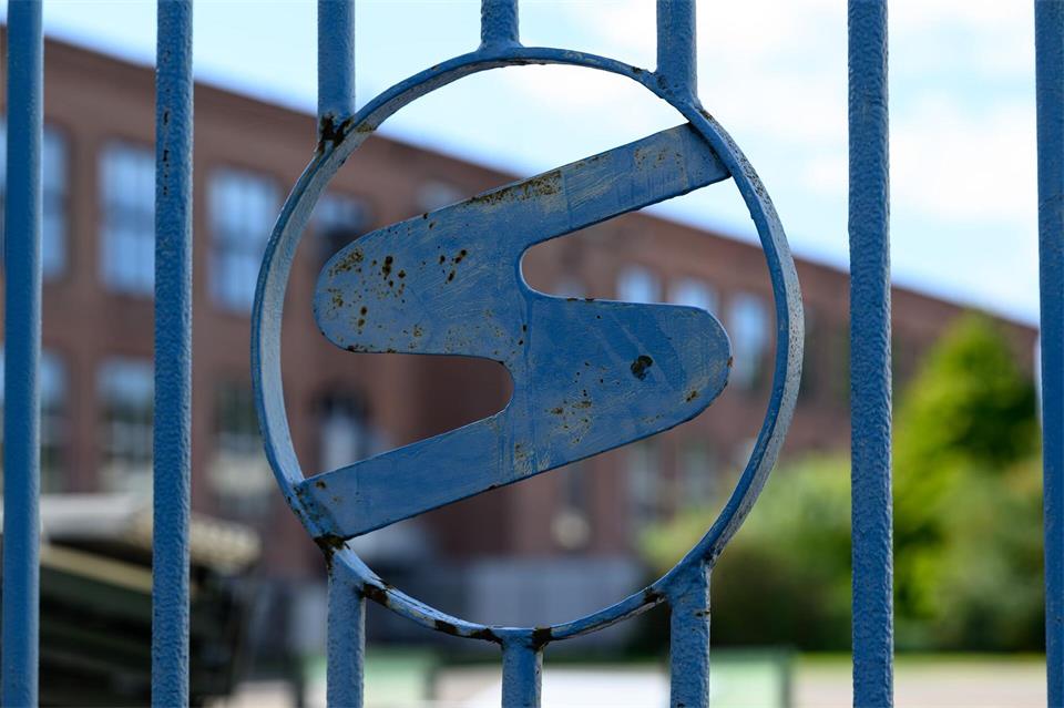 Das Sachsenring-Logo ist in einem Zaun nahe der früheren Endmontage des Trabant in Zwickau zu sehen. Hendrik Schmidt/dpa
