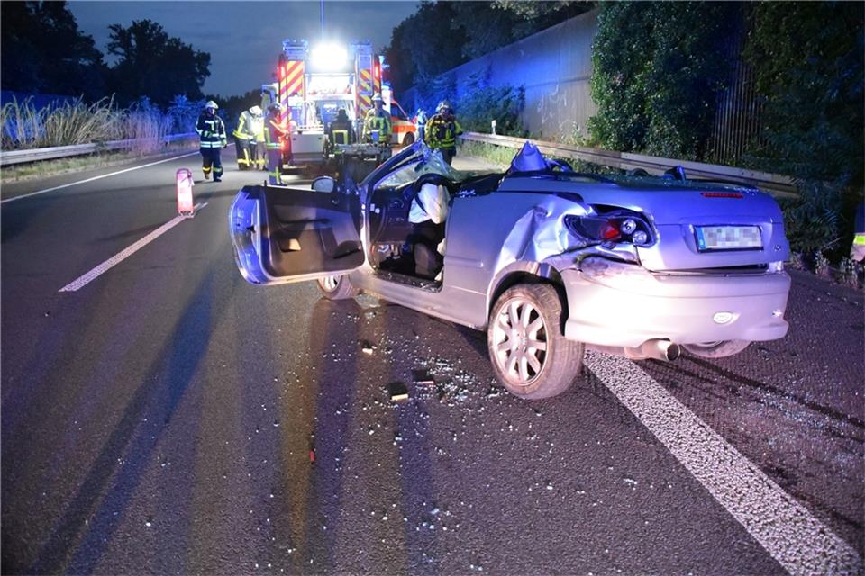 Das zerstörte Fahrzeug steht nach dem Unfall auf der Autobahn A57, im Hintergrund arbeiten Rettungskräfte.