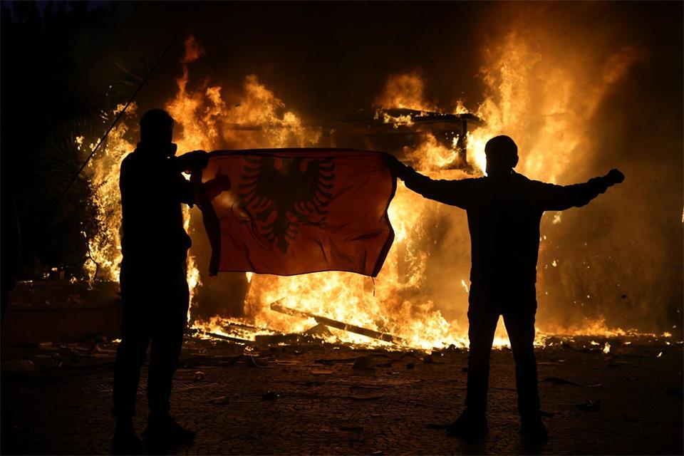 Demonstranten halten während Ausschreitungen in Tirana eine albanische Fahne vor einem brennenden Tabakladen hoch, als sich Studenten einer regierungsfeindlichen Demonstration anschließen.Hameraldi Agolli/AP/dpa
