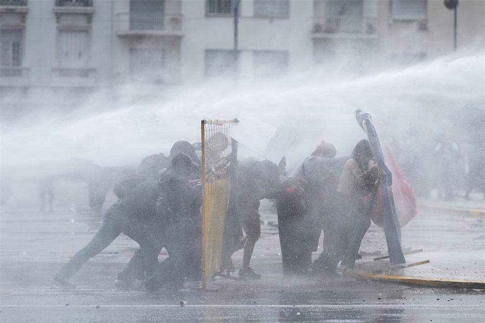 Demonstranten in Buenos Aires suchen Deckung, während die Polizei bei einer regierungskritischen Demonstration einen Wasserwerfer einsetzt.Rodrigo Abd/AP/dpa