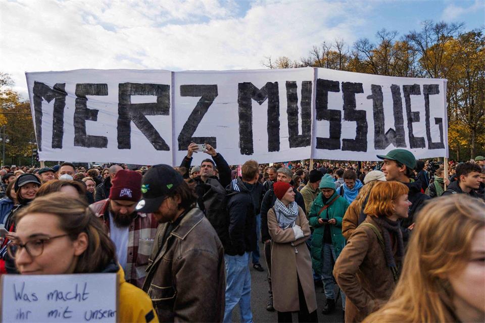 Demonstrations-Teilnehmer halten ein Banner mit dem Text „Merz muss weg“. Carsten Koall/dpa