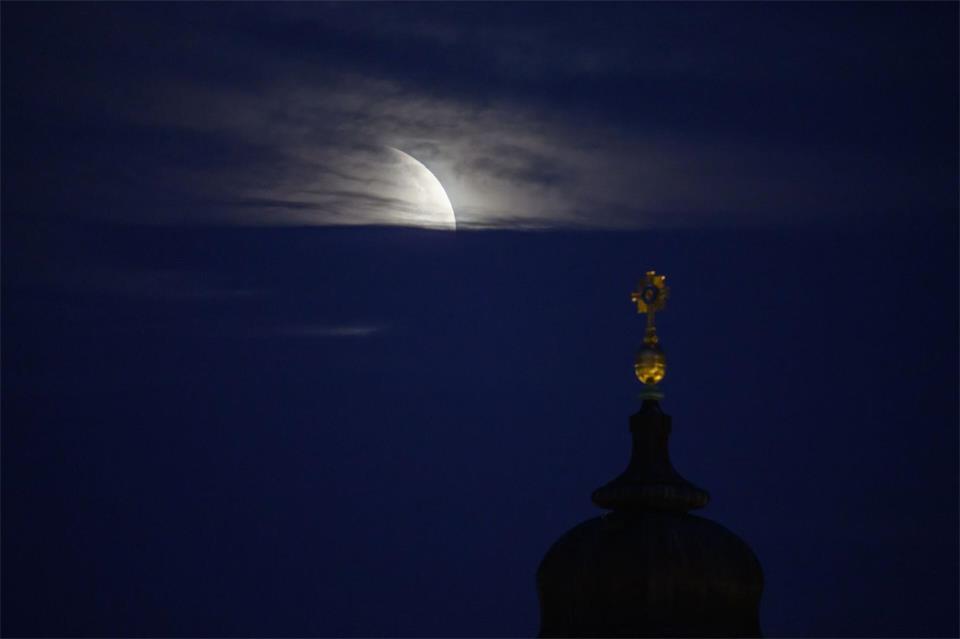 Der Mond geht am Morgen während einer partiellen Mondfinsternis hinter dem Kreuz der Frauenkirche unter. Robert Michael/dpa