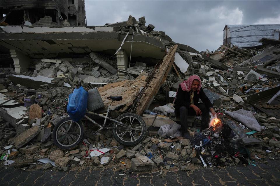 Der Palästinenser Mohammed al-Jabri, 58, wärmt sich neben einem Feuer, während er auf den Trümmern eines Gebäudes sitzt, das während der israelischen Luft- und Bodenoperationen im Viertel Sheikh Radwan zerstört wurden.Abdel Kareem Hana/AP/dpa