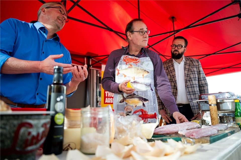 Der Thüringer Umweltminister Tilo Kummer (BSW) bereitet gemeinsam mit dem Präsidenten des Thüringer Fischereiverbands, Torsten Schmidt (l), und dem Geschäftsführer der RAM Regio Ausstellung GmbH, Robert Ninnemann (r), den Fisch für den Grill vor.Jacob Schröter/dpa