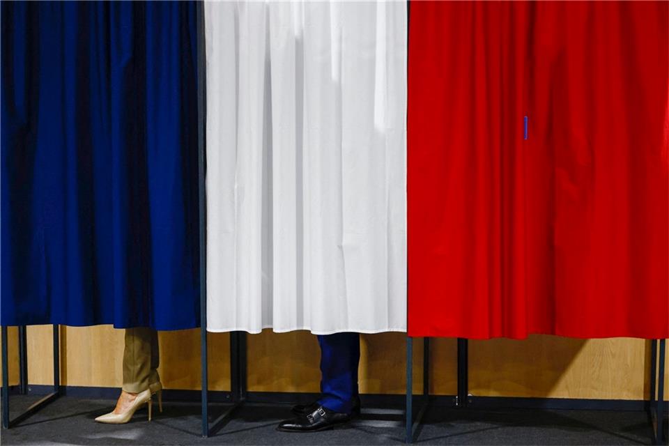 Wahl in Frankreich: Rechtsnationale könnten Mehrheit holen Der französische Präsident Emmanuel Macron und seine Frau Brigitte Macron stehen vor der Stimmabgabe in der Wahlkabine.