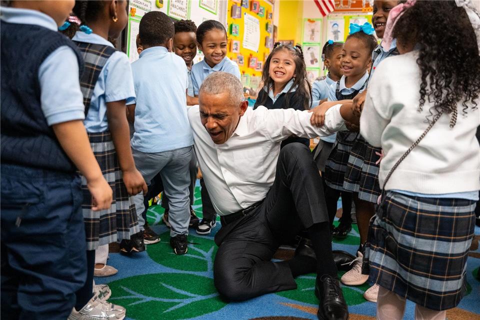Der frühere US-Präsident Barack Obama lässt sich beim Aufstehen von Kindern hochheben.Angelina Katsanis/AP/dpa