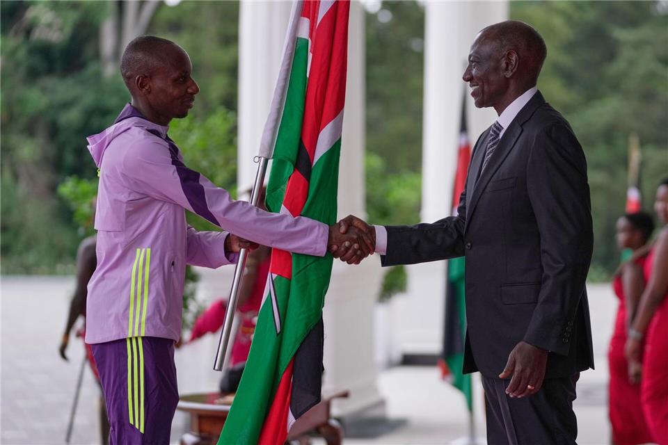 Der kenianische Marathon-Weltrekordler Sabastian Sawe (l) übergibt die kenianische Flagge an Präsident William Ruto.Brian Inganga/AP/dpa