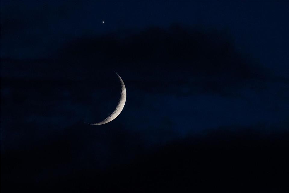 Der sichelförmige Mond wird am Abend hinter Wolken über Köln von der Venus (oben) begleitet.Rolf Vennenbernd/dpa