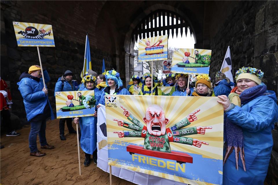 Der ukrainische Hilfsverein Blau-Gelbes-Kreuz hält Plakate mit Putin-Motiven hoch. Das ist als Zeichen der Solidarität mit Wagenbauer Jacques Tilly gemeint. Dieser wird in Russland strafrechtlich verfolgt. Oliver Berg/dpa