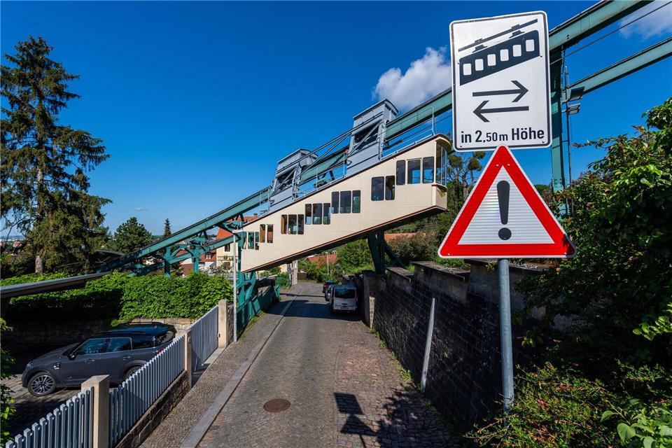 Die 1901 gebaute Schwebebahn fährt zum Dresdner Stadtteil Oberloschwitz über einer Straße an einem Warnschild vorbei. (Archivbild)Robert Michael/dpa-Zentralbild/dpa
