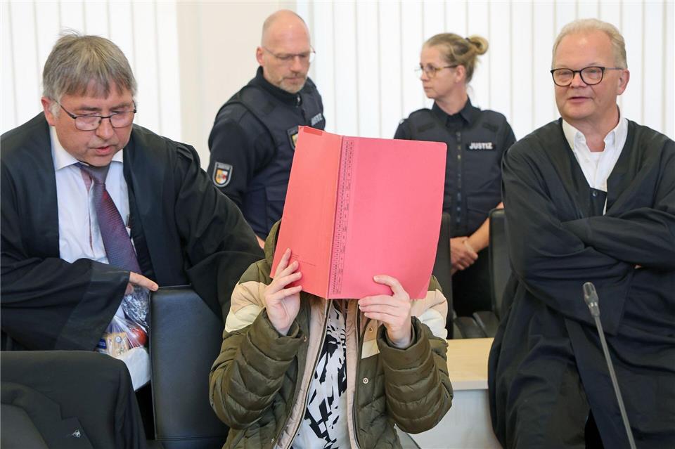 Die Angeklagte sitzt mit Aktendeckel vor dem Gesicht zwischen ihren Verteidigern Andreas Ohm (l-r) und Thomas Löcker. Bernd Wüstneck/dpa