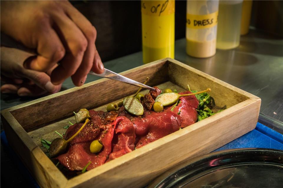 Die Carpaccio-Scheiben werden auf dem Rucola-„Gebirge“ angerichtet und mit Oliven, Kapernäpfeln und getrockneten Tomaten getoppt - immer dort, wo der Berg kleine Täler hinterlassen hat. Christin Klose/dpa-tmn