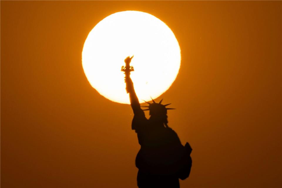 Die Freiheitsstatue in New York zeichnet sich vor der untergehenden Sonne ab.Yuki Iwamura/AP/dpa