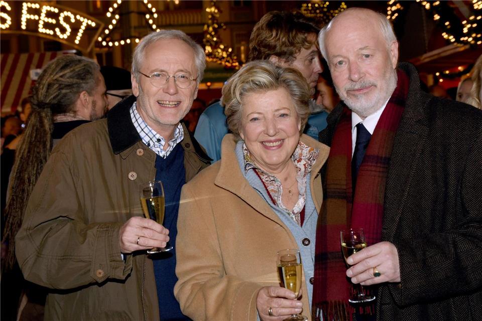 Die Schauspieler Joachim Hermann Luger (Hans Beimer, links) und die Schauspieler Marie-Luise Marjan (Mutter Beimer) und Bill Mockridge (Erich Schiller, rechts) posieren in der Außenkulisse mit Sektgläsern nach der Live-Ausstrahlung der 1559. Folge im Dezember 2015.picture alliance / dpa