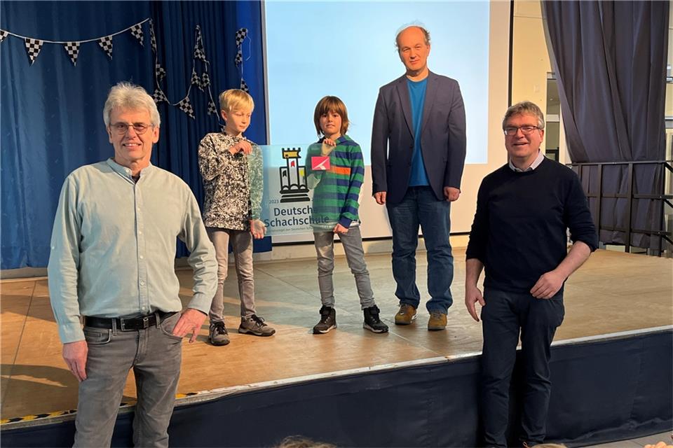 Die Schüler Ole (links) und Enno nehmen das neue Schulschild entgegen, das Helge Frowein, Referent der Deutschen Schachjugend, mitgebracht hat. Schulleiter Thomas Schlüter (rechts) und Konrektor Manfred Grömping freuen sich sehr über das Siegel in Gold, mit dem das umfangreiche Schachangebot der St.-Sebastian-Grundschule auszeichnet wird.