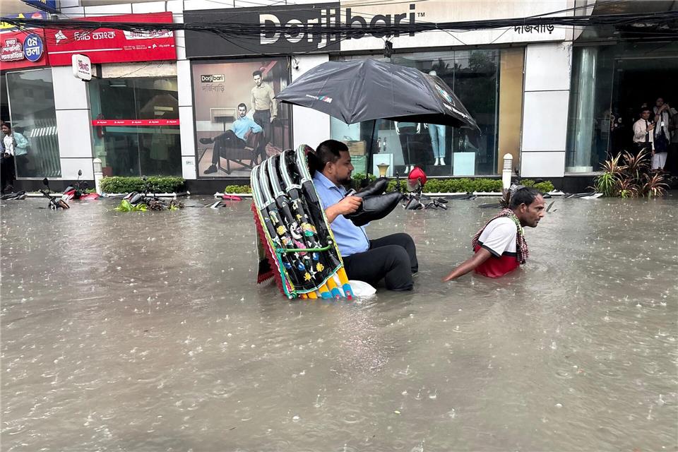 Die Schuhe bleiben trocken: Ein Mann lässt sich in Bangladesch in einer Rikscha durch eine überflutete Straße fahren. -/XinHua/dpa