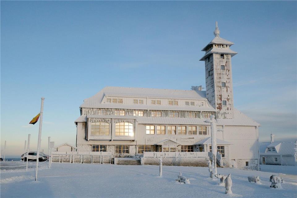 Die aufgehende Sonne spiegelt sich in den Fenstern des vereisten Fichtelberghauses. Sebastian Willnow/dpa