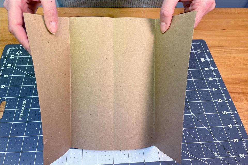 Die kurze Seite des Kraftpapiers mittig nach oben falten und anschließend wieder aufklappen. Nun die Enden jeweils bis zur Falz klappen, sodass vier gleich breite Abschnitte entstehen.DIY Academy/dpa-tmn