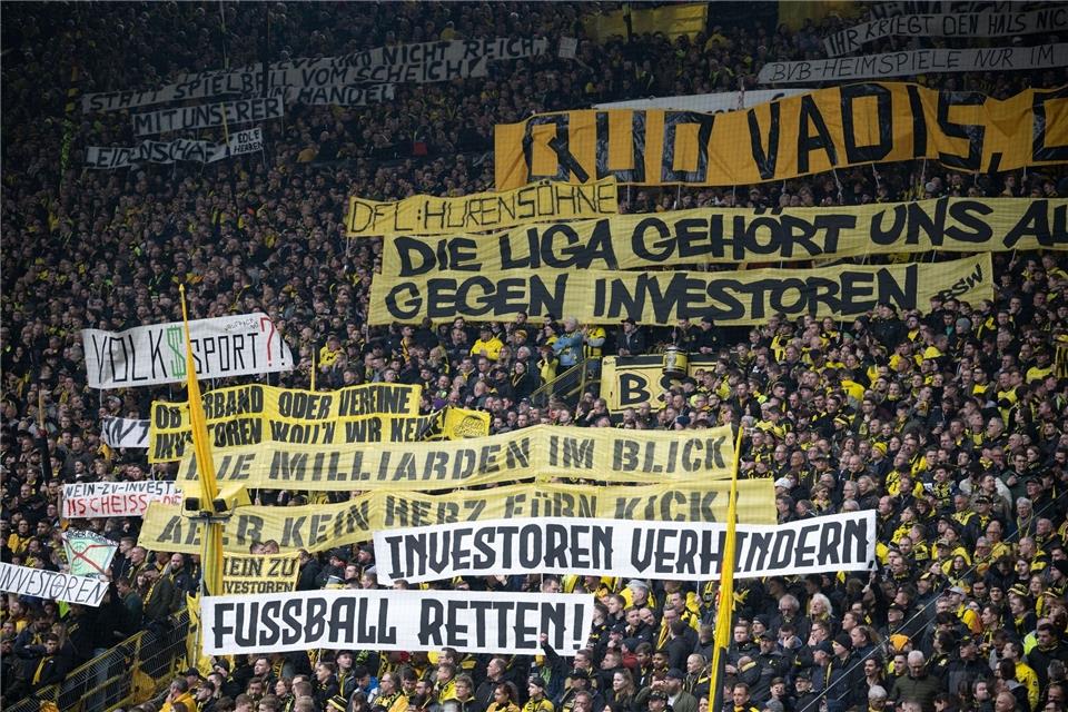 Dortmunds Fans protestieren gegen Investoren im Fußball mit Transparenten mit den Aufschriften: „DFL Hurensöhne“, „Die Liga gehört uns ...“, „Gegen Investoren“, „Die Milliarden im Blick“, „Kein Herz fürn Kick“, „Investoren verhindern“ sowie „Fußball retten“.