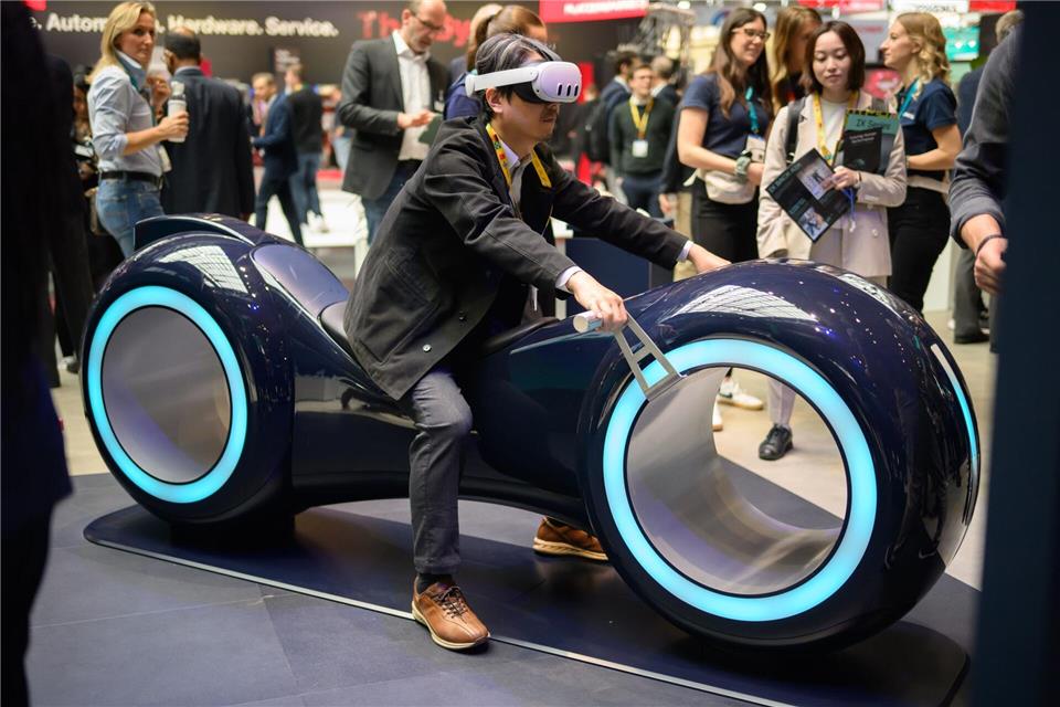 Durch eine Augmented-Reality-Brille schauend sitzt ein Gast auf einem fiktiven Gefährt bei der Industriemesse Hannover.Julian Stratenschulte/dpa